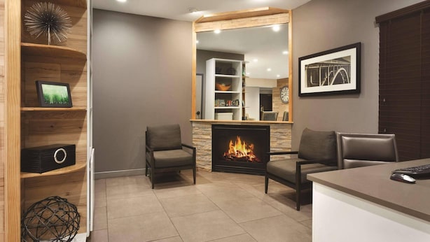 A modern living room with a fireplace, two armchairs, a coffee table, and a bookshelf.