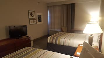 A hotel room with two beds, a TV on a dresser, a lamp, and framed pictures on the wall.