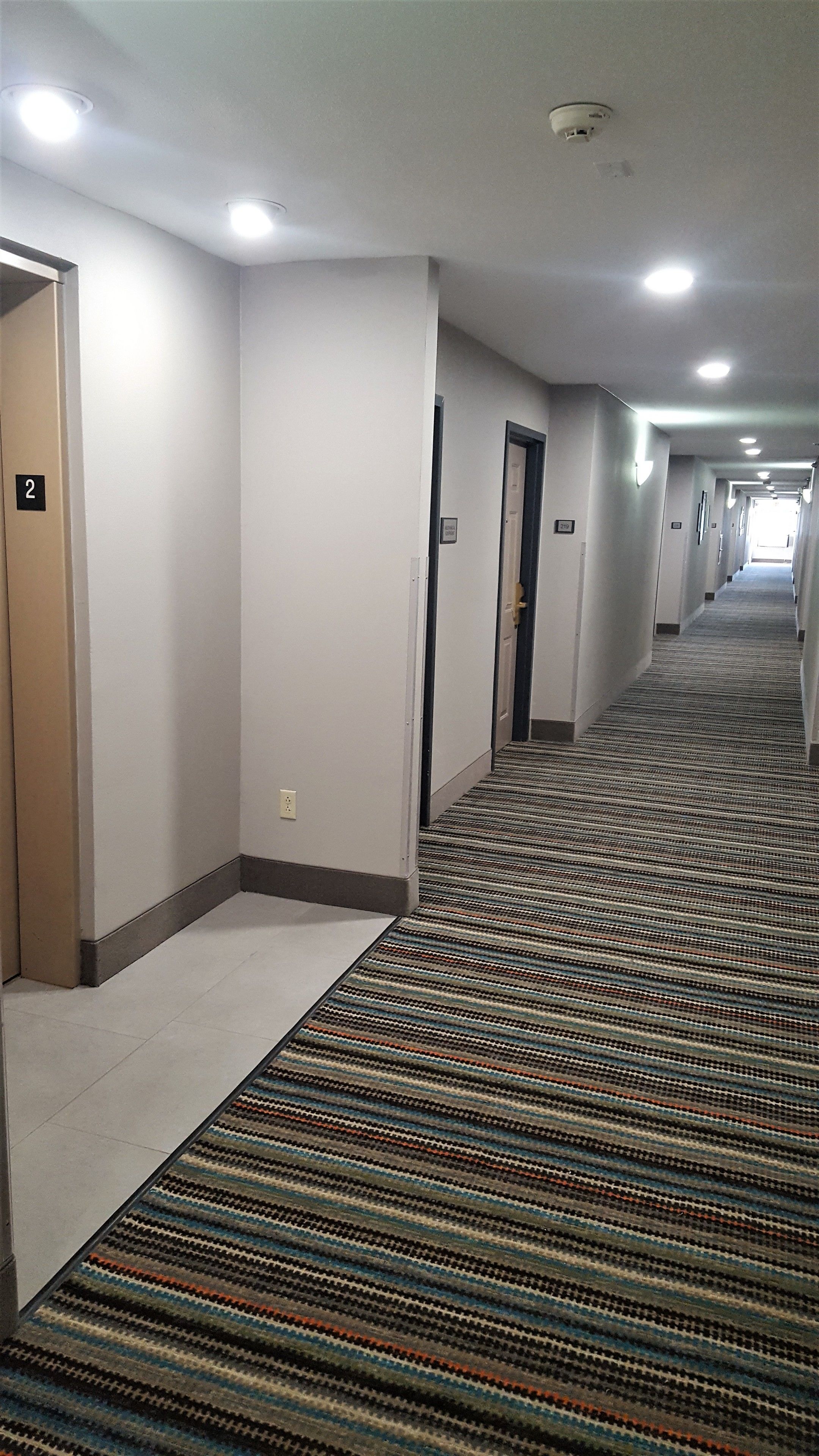 Corredor de hotel com piso coberto por carpete, portas e iluminação embutida.
