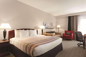 A hotel room with a large bed, two bedside tables with lamps, a desk, a red armchair, and a black office chair.