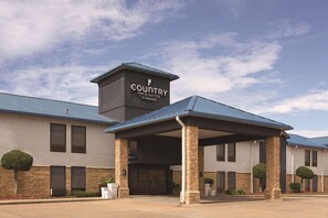 A Country Inn & Suites building with a covered entrance, stone facade, and a clear sky.