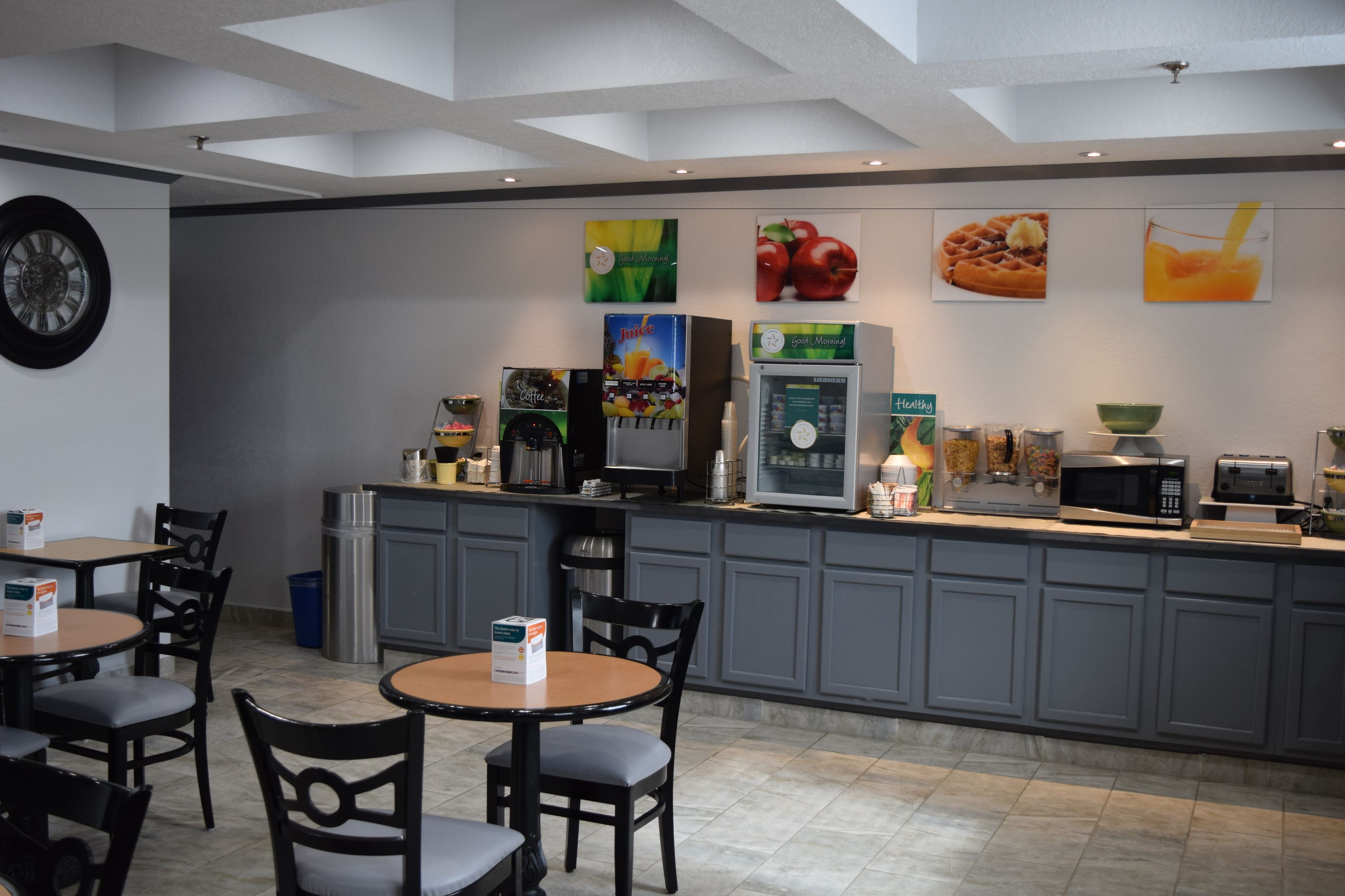A modern kitchen area with a coffee machine, microwave, and toaster. There are chairs and tables for dining.