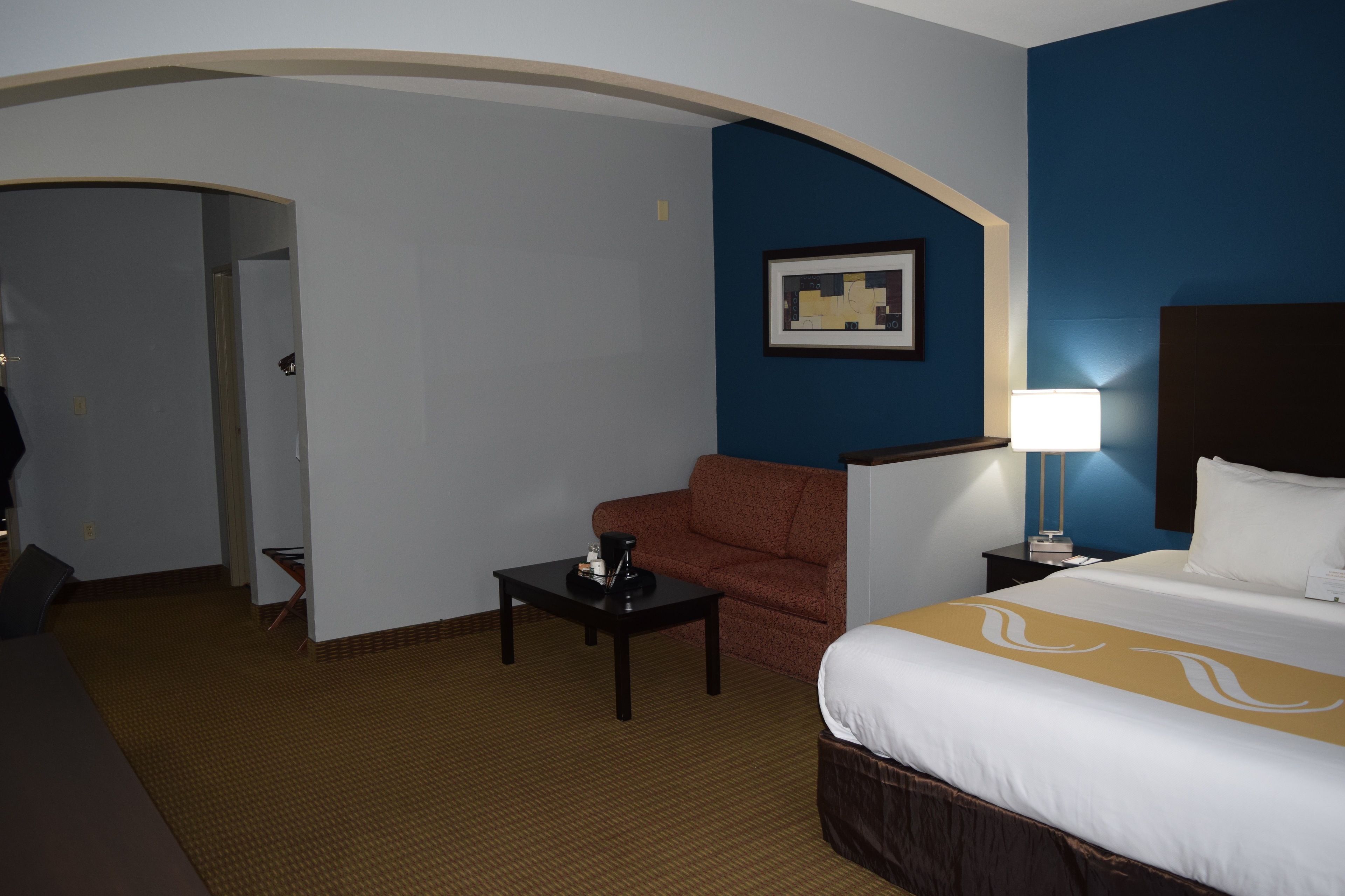 A hotel room with a bed, a sofa, a coffee table, a lamp, and a framed picture on the wall.