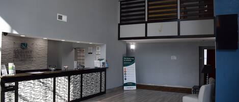 A reception area with a counter, a signboard, a chair, and a staircase.
