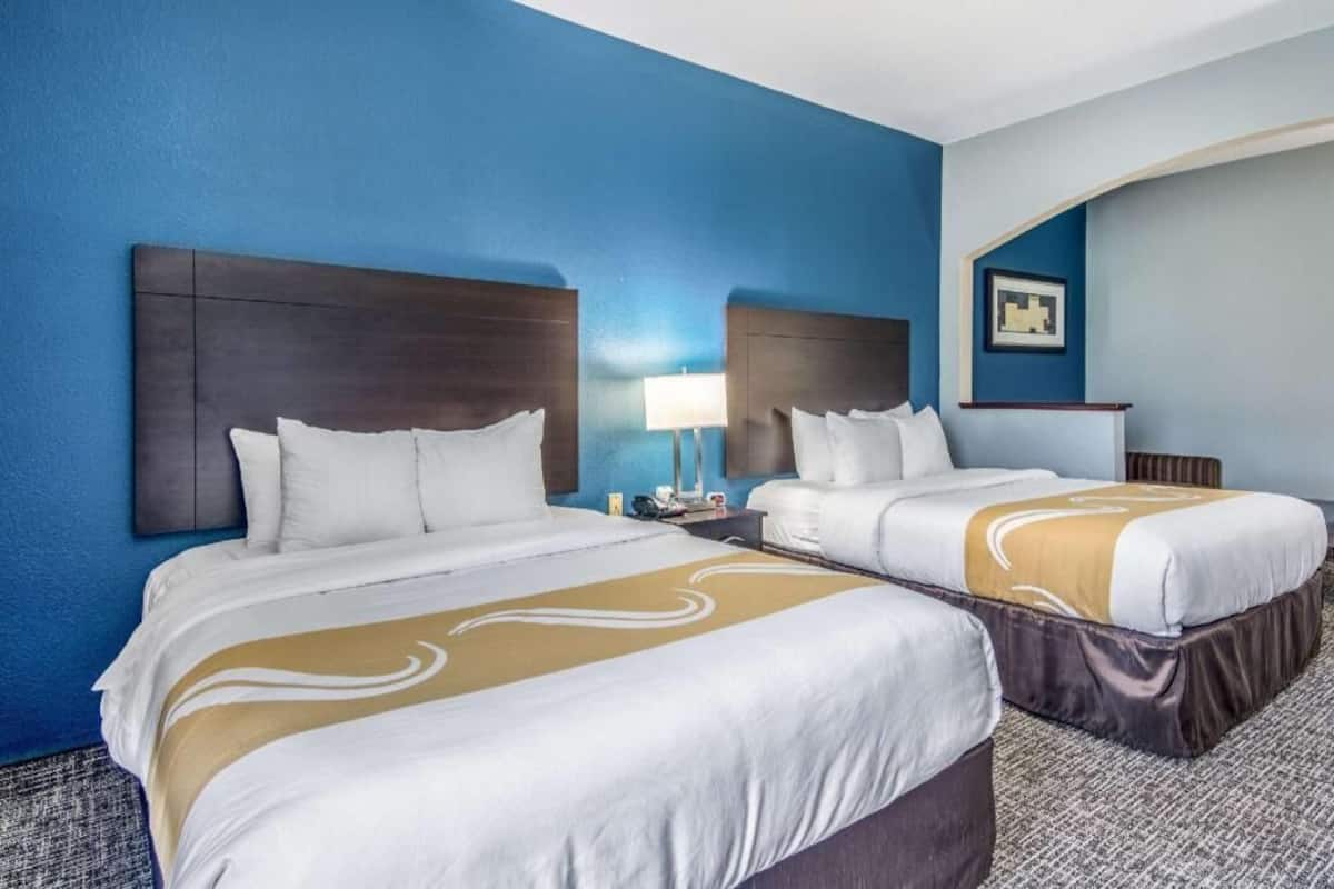 A hotel room with two beds, a nightstand, a lamp, and a framed picture on the wall.