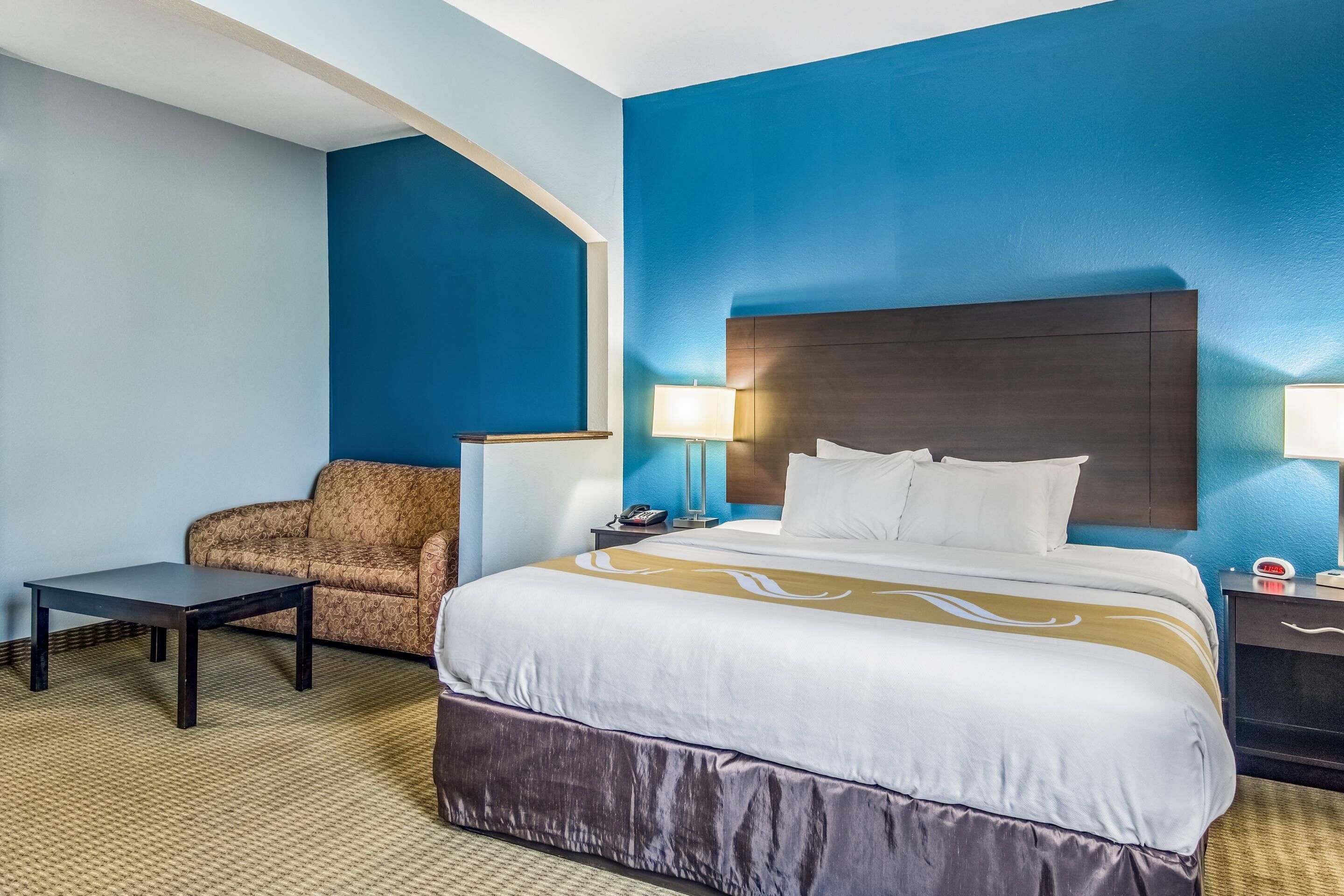 A hotel room with a large bed, a sofa, a small table, and two bedside lamps.