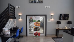 Un espacio de oficina moderno con un mostrador de recepción, sillas de oficina azules, una escalera y una puerta de cristal con un cartel publicitario de desayuno.