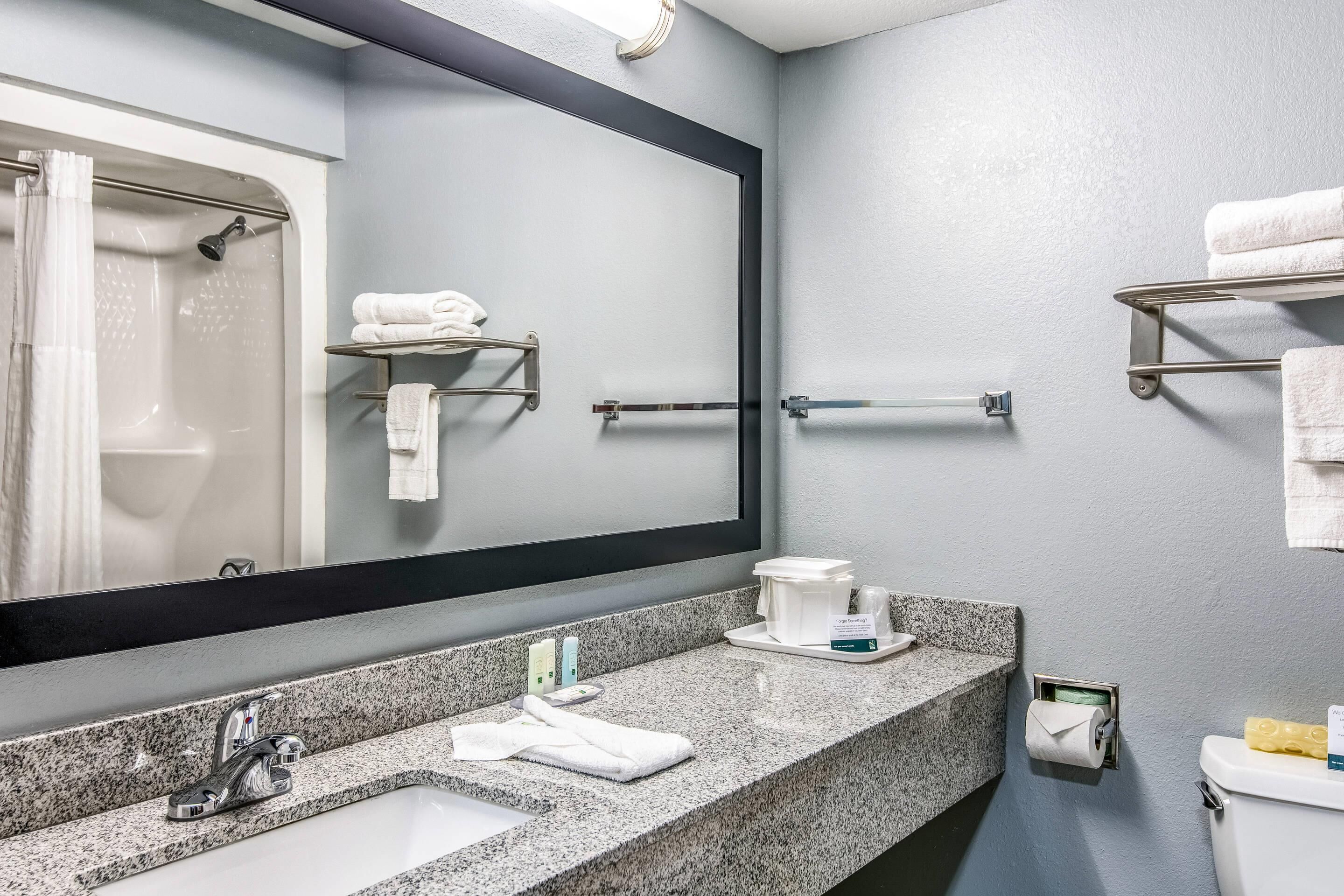 A modern bathroom with a granite countertop, a sink, a mirror, a shower, and towel racks.