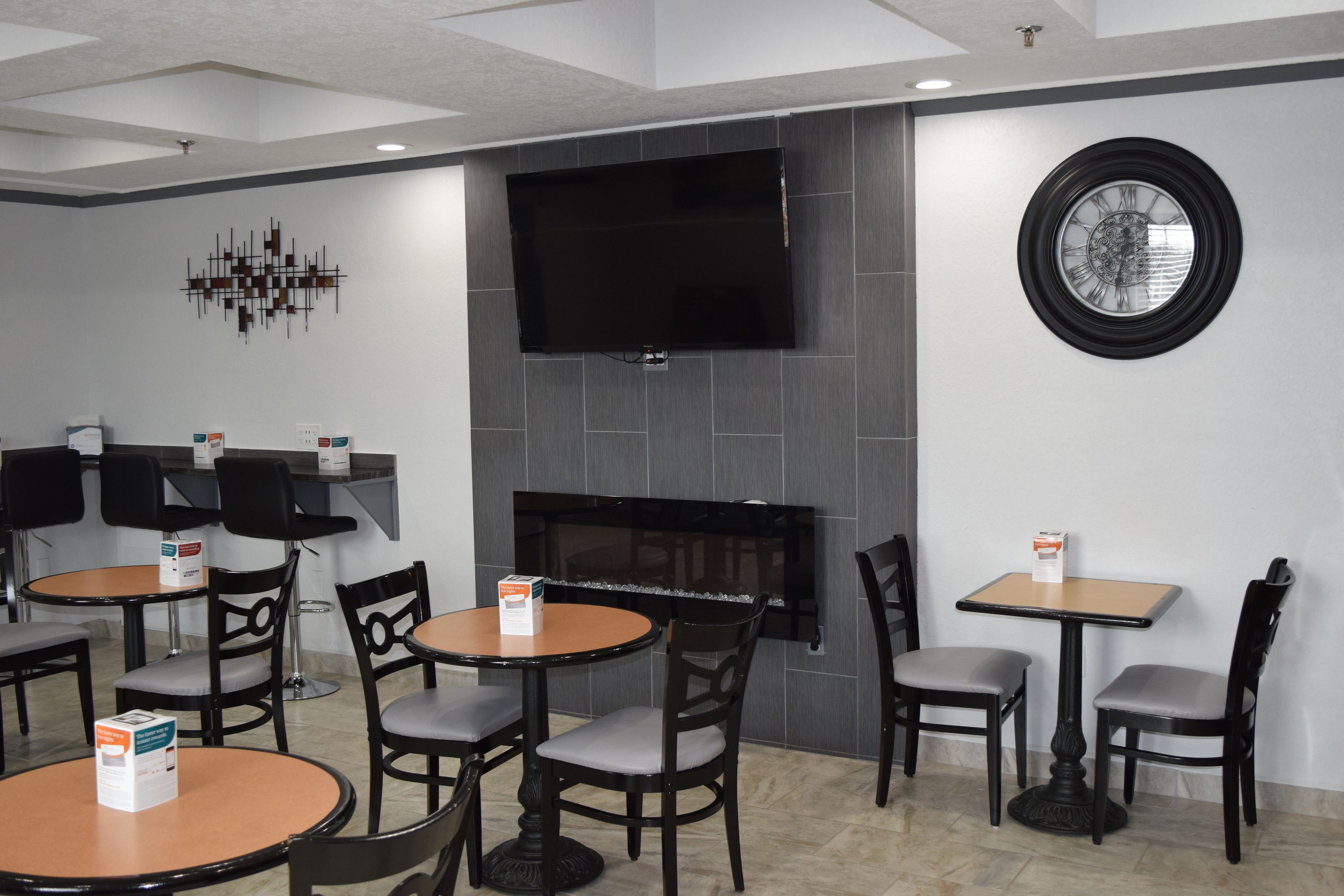 Un restaurante con varias mesas y sillas, un televisor de pantalla plana montado en la pared y un reloj decorativo.