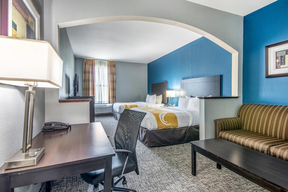 A hotel room with a desk, two beds, a sofa, and a TV.