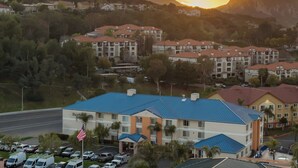 Um hotel com telhado azul, cercado por carros estacionados e palmeiras.