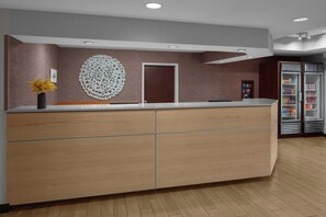 Un espace d’accueil comprenant un comptoir de réception en bois, un élément décoratif mural, une porte et un réfrigérateur rempli de boissons.