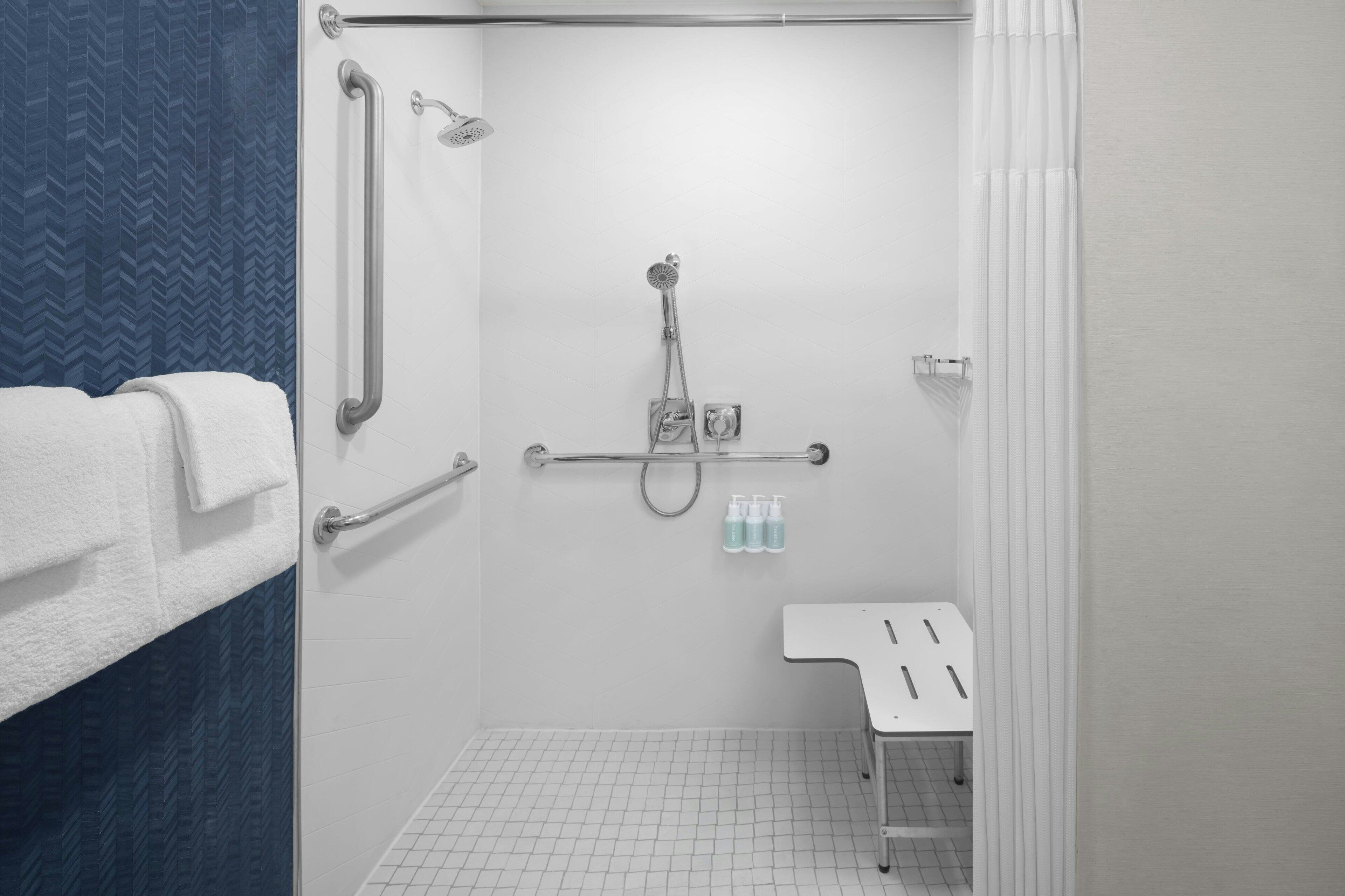 Un baño moderno con ducha, barras de apoyo, un lavamanos blanco y un perchero para toallas.