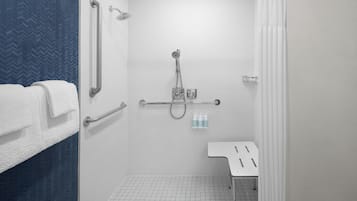 A modern bathroom with a shower, grab bars, a white sink, and a towel rack.