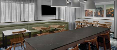 Una habitación de hotel moderna con una amplia mesa de comedor, sillas de madera, un sofá verde y un televisor colgado en la pared.