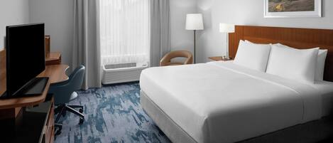Habitación de hotel con una cama grande, un escritorio con computadora, una silla, una lámpara y una ventana con cortinas.