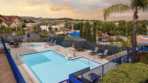 Uma piscina com cerca azul, cadeiras de descanso e vista para o bairro ao redor.