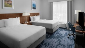 Quarto de hotel com duas camas, uma escrivaninha com computador, uma cadeira e uma janela grande com cortinas.