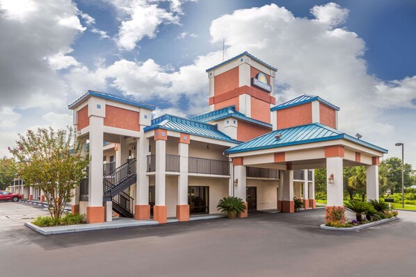 Stylish hotel with a central tower, covered entrance, and balconies, set amidst landscaped gardens and a parking area.