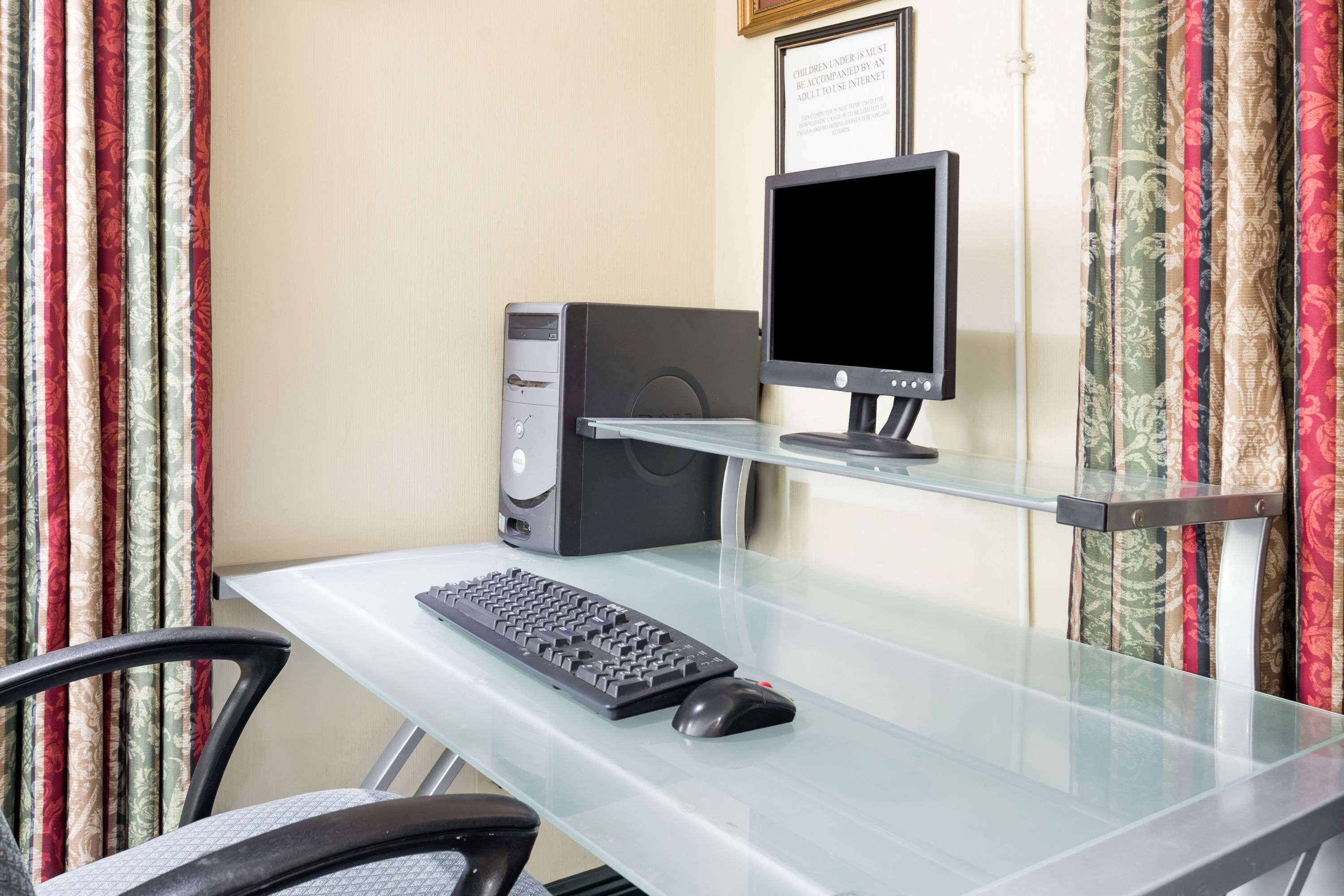 Uma mesa de computador com teclado, rato e monitor, um computador de mesa e um aviso emoldurado na parede.
