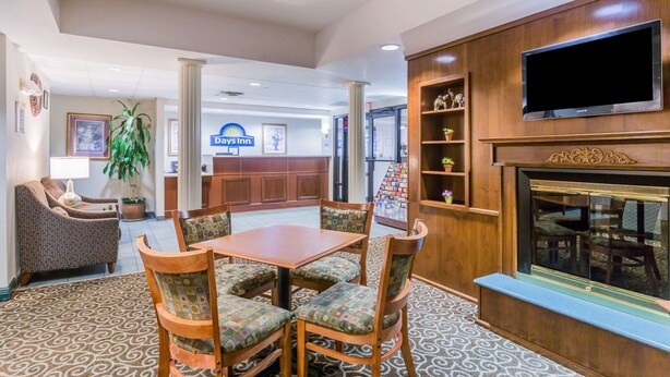 A hotel lobby with a reception desk, a dining area with a table and chairs, a flat-screen TV mounted on the wall, and a fireplace. - Days Inn by Wyndham Chiefland (Chiefland)
