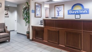 A reception area with a Days Inn sign, a reception desk, framed pictures on the wall, a potted plant, and a patterned armchair. - Days Inn by Wyndham Chiefland (Chiefland)