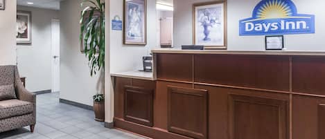 Een receptiegedeelte met een Days Inn bord, een receptiebalie, ingelijste foto’s aan de muur, een potplant en een gestreept fauteuil.