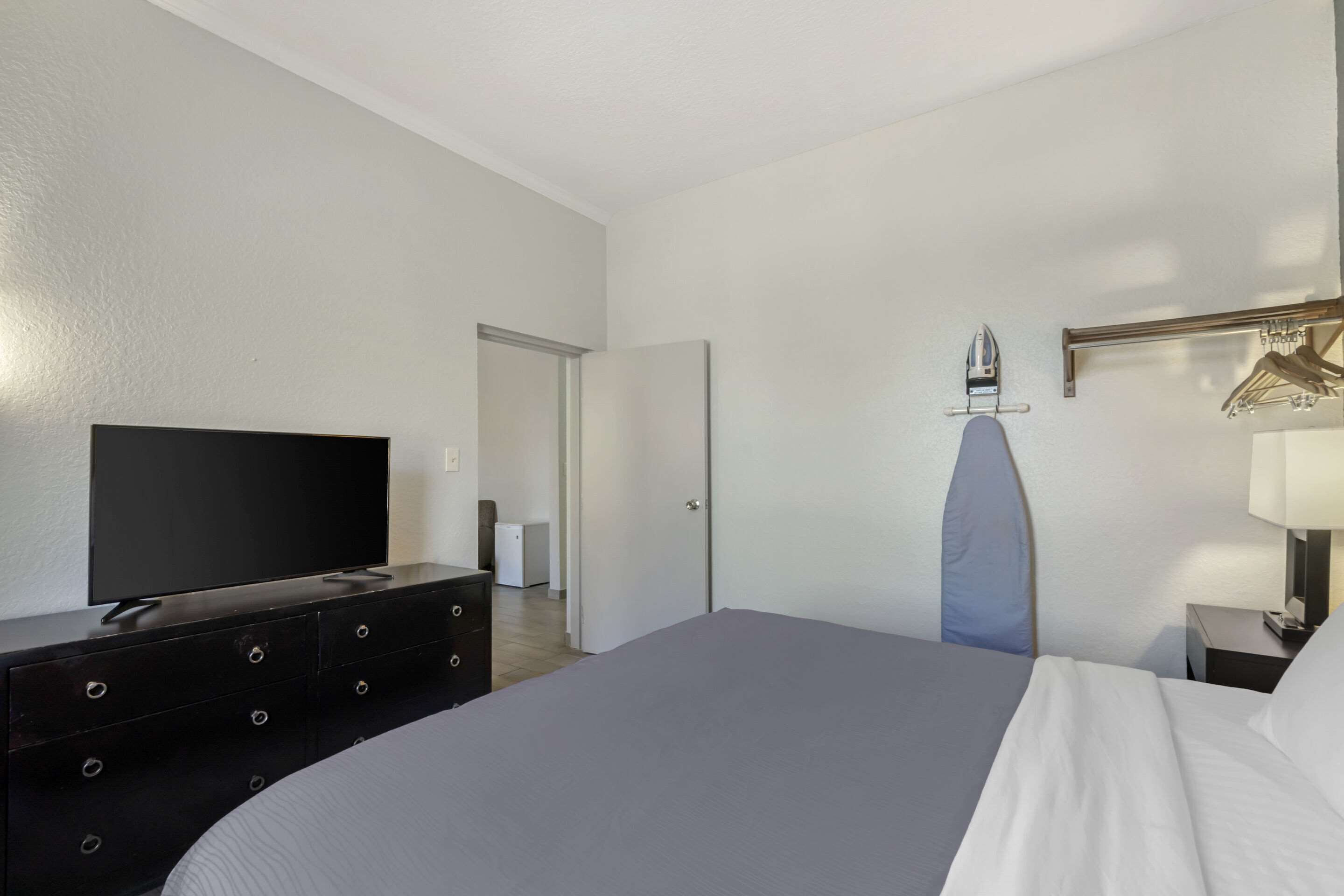 Quarto de hotel com cama, cômoda, televisão, espelho e porta que dá para outro quarto.
