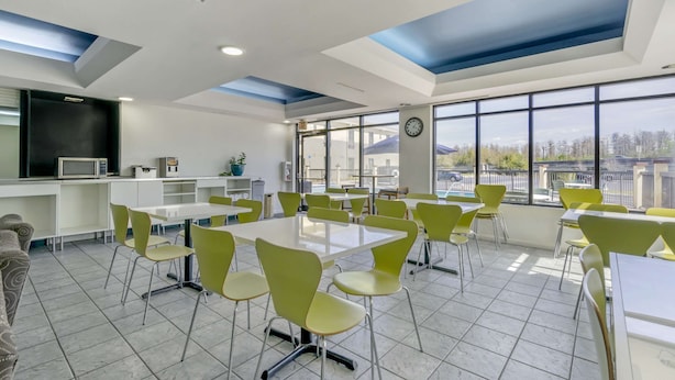 A spacious dining area with high tables and green chairs, large windows with a city view, and a modern ceiling design. - Rodeway Inn Wesley Chapel (Wesley Chapel)