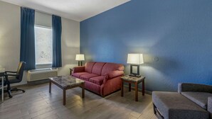 A room with a red sofa, two side tables with lamps, a wooden coffee table, a chair, and a window with blue curtains. - Rodeway Inn Wesley Chapel (Wesley Chapel)