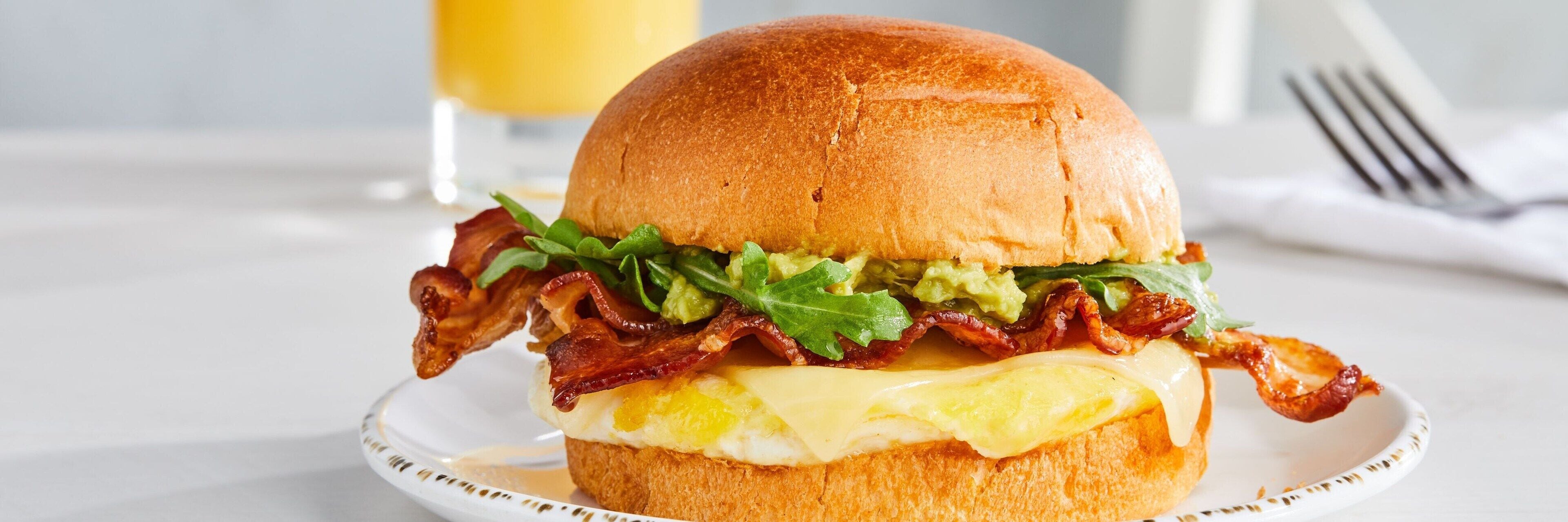 En frukostmacka med bacon, sallad och ost på ett bröd.