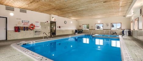 Piscina interior con techo de madera, señales de seguridad y una silla de salvavidas.