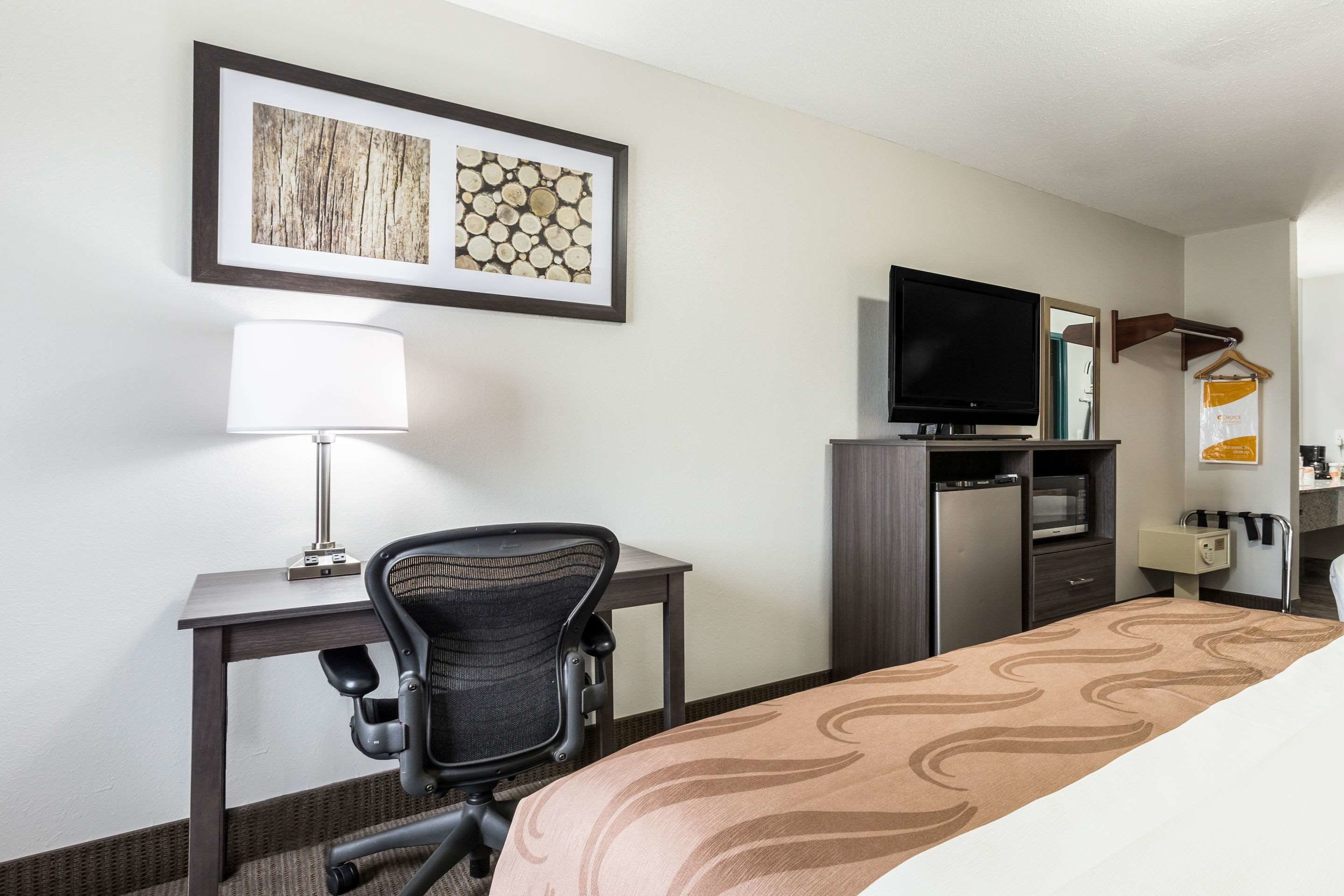 A hotel room with a bed, a desk with a chair, a TV, a microwave, and a small kitchenette.