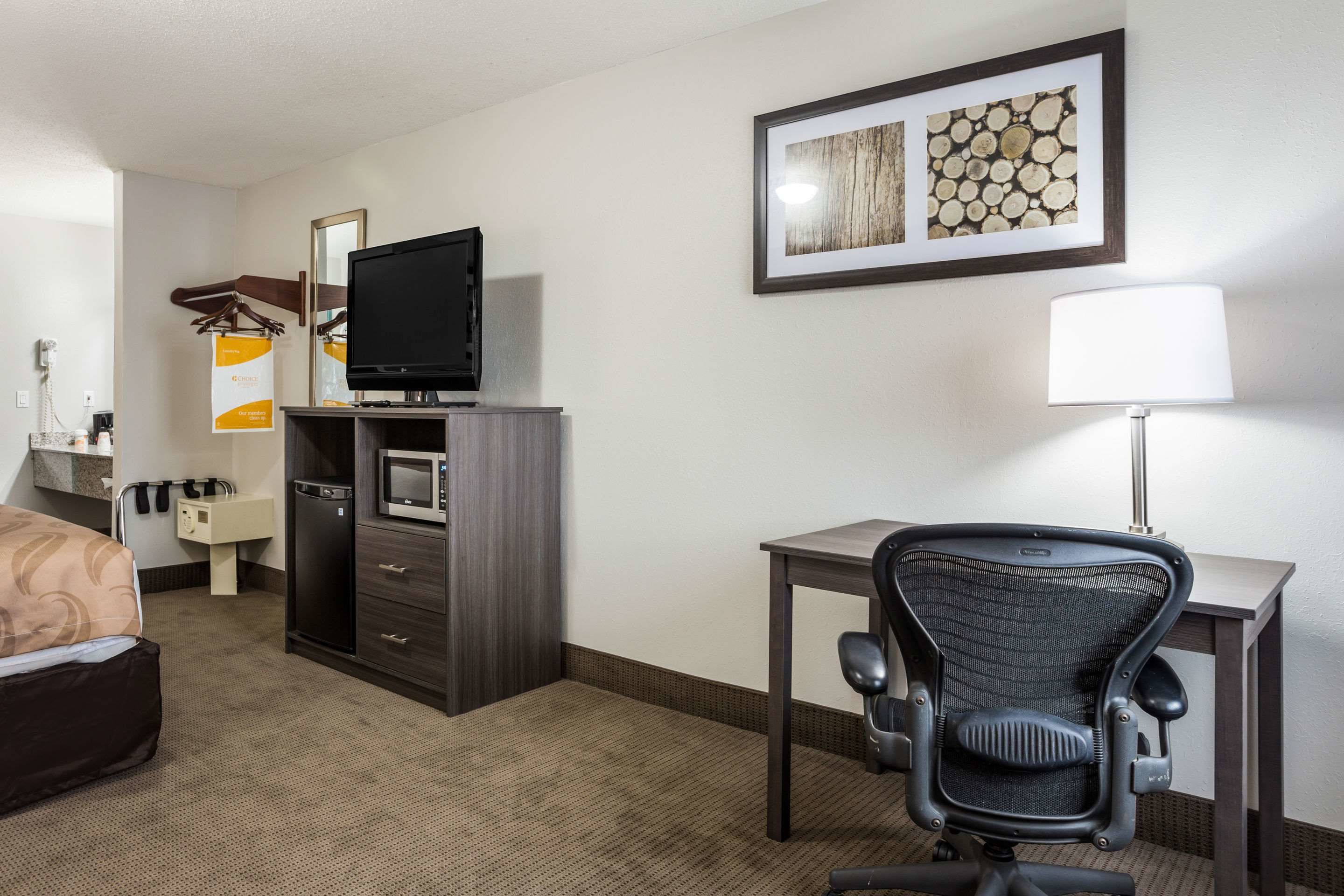 A hotel room with a bed, a desk with a chair, a television, a lamp, and a framed picture on the wall.