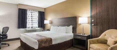 A hotel room with a large bed, two bedside lamps, a chair, a desk, and a window with curtains.