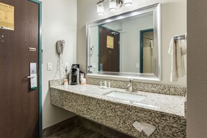 A bathroom with a granite countertop, sink, and mirror. There is a towel rack with towels, a hairdryer, and a phone on the wall.