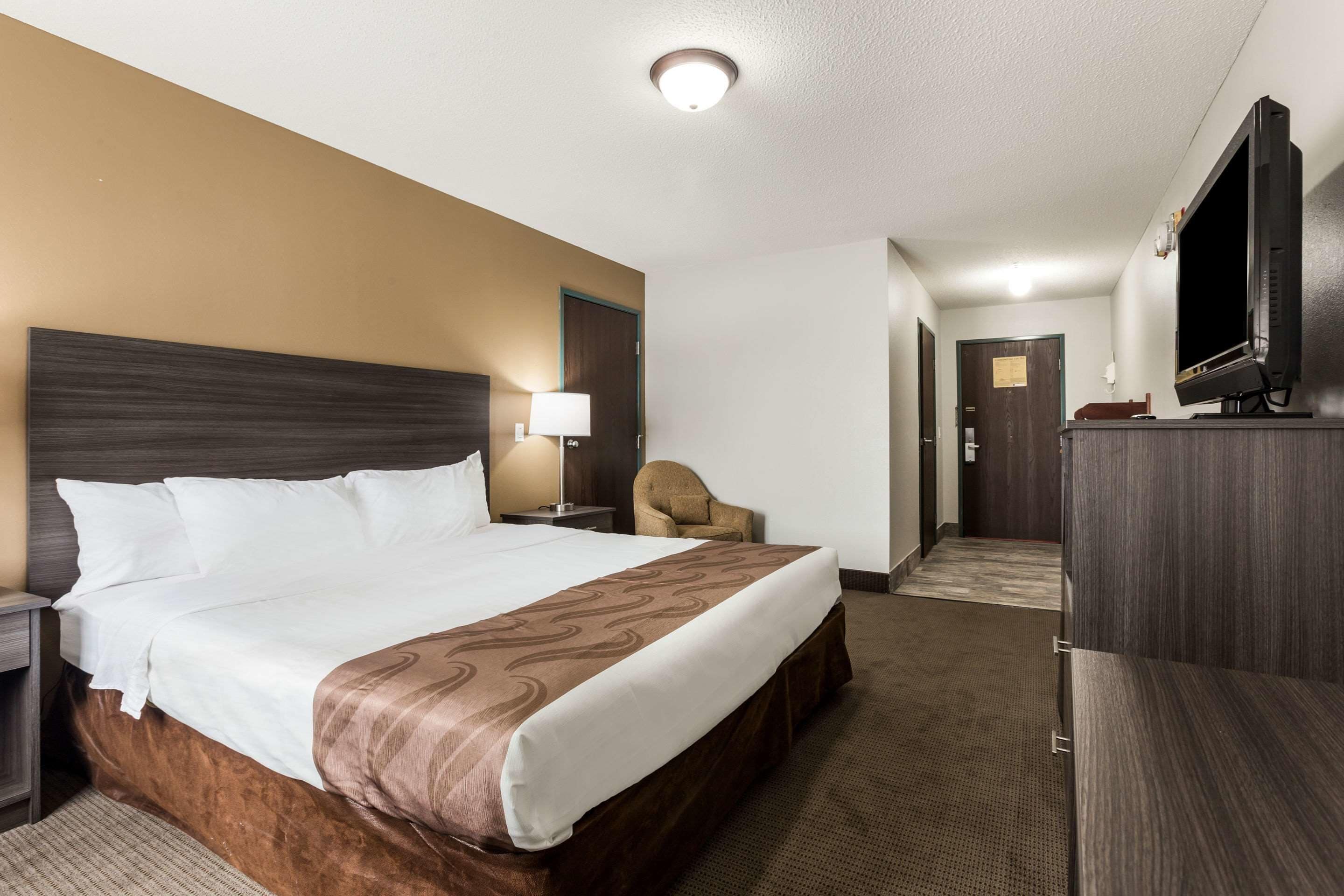 A hotel room with a large bed, a TV, a chair, and a desk.