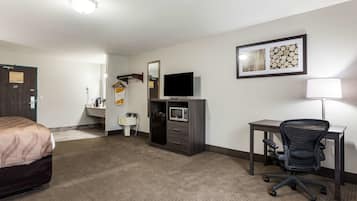 A hotel room with a bed, a desk, a chair, a television, a microwave, and a mirror.