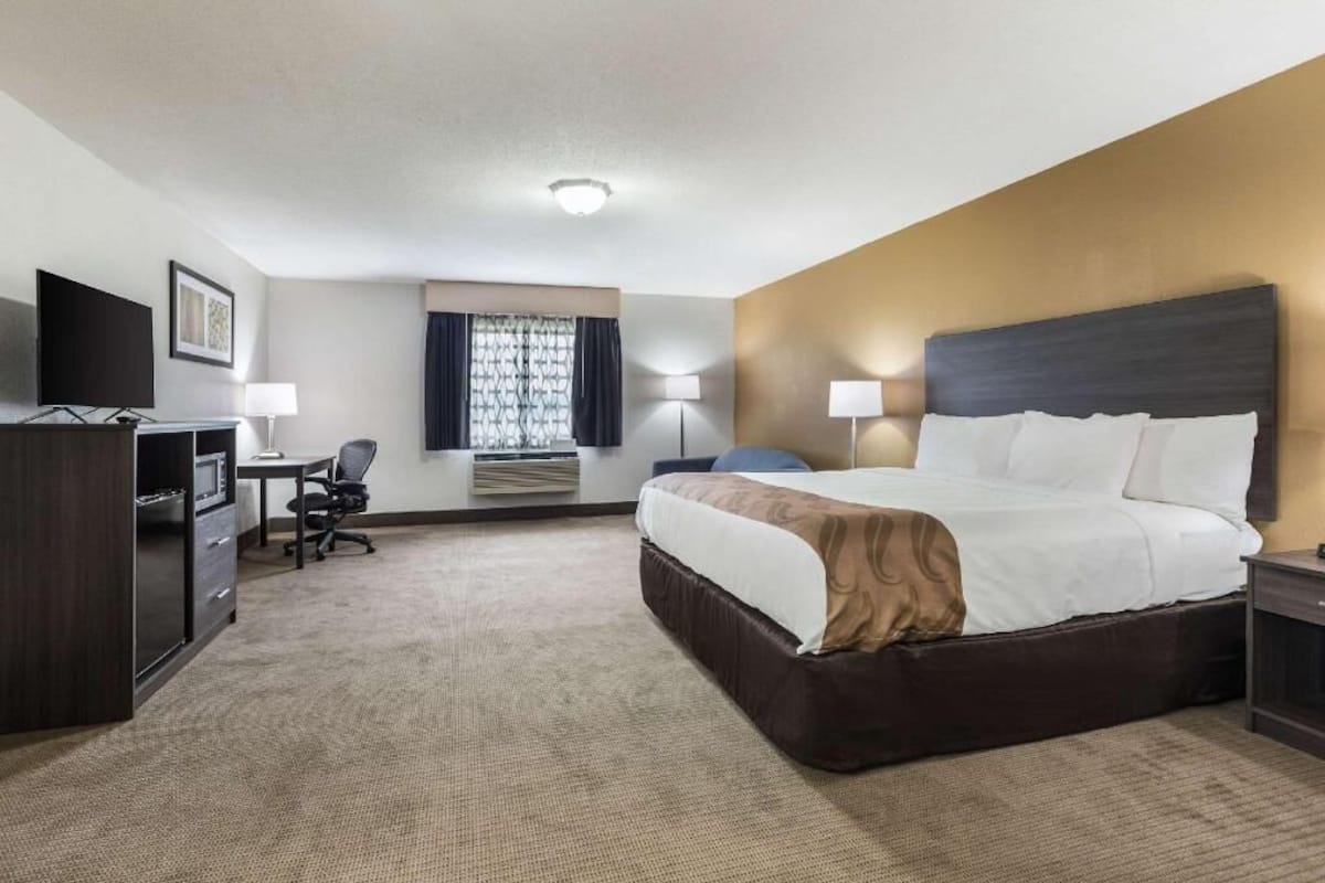Habitación de hotel con cama, escritorio, silla, televisor y ventana con cortinas.