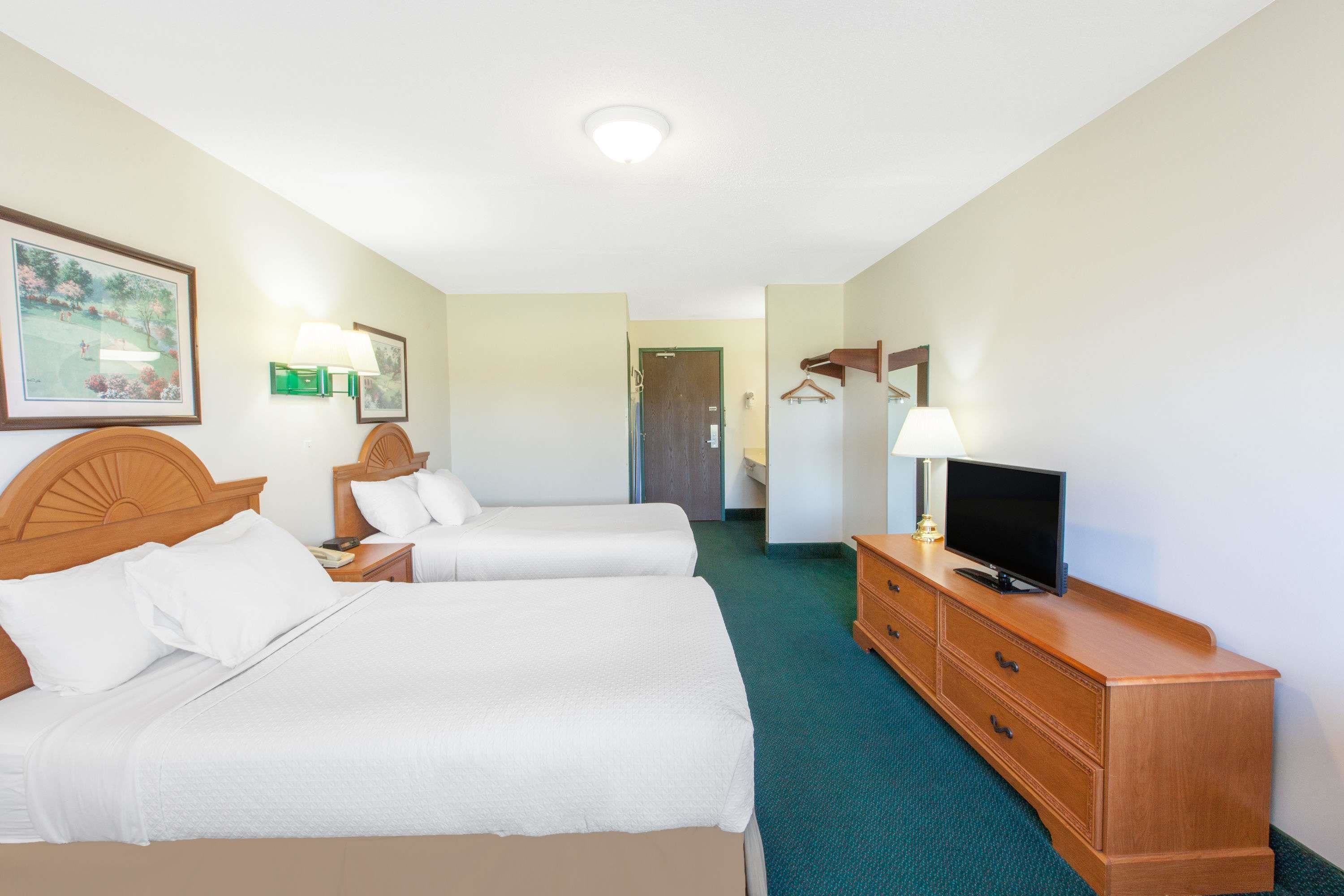 A hotel room with two beds, a television, a dresser, and a hallway leading to a door.