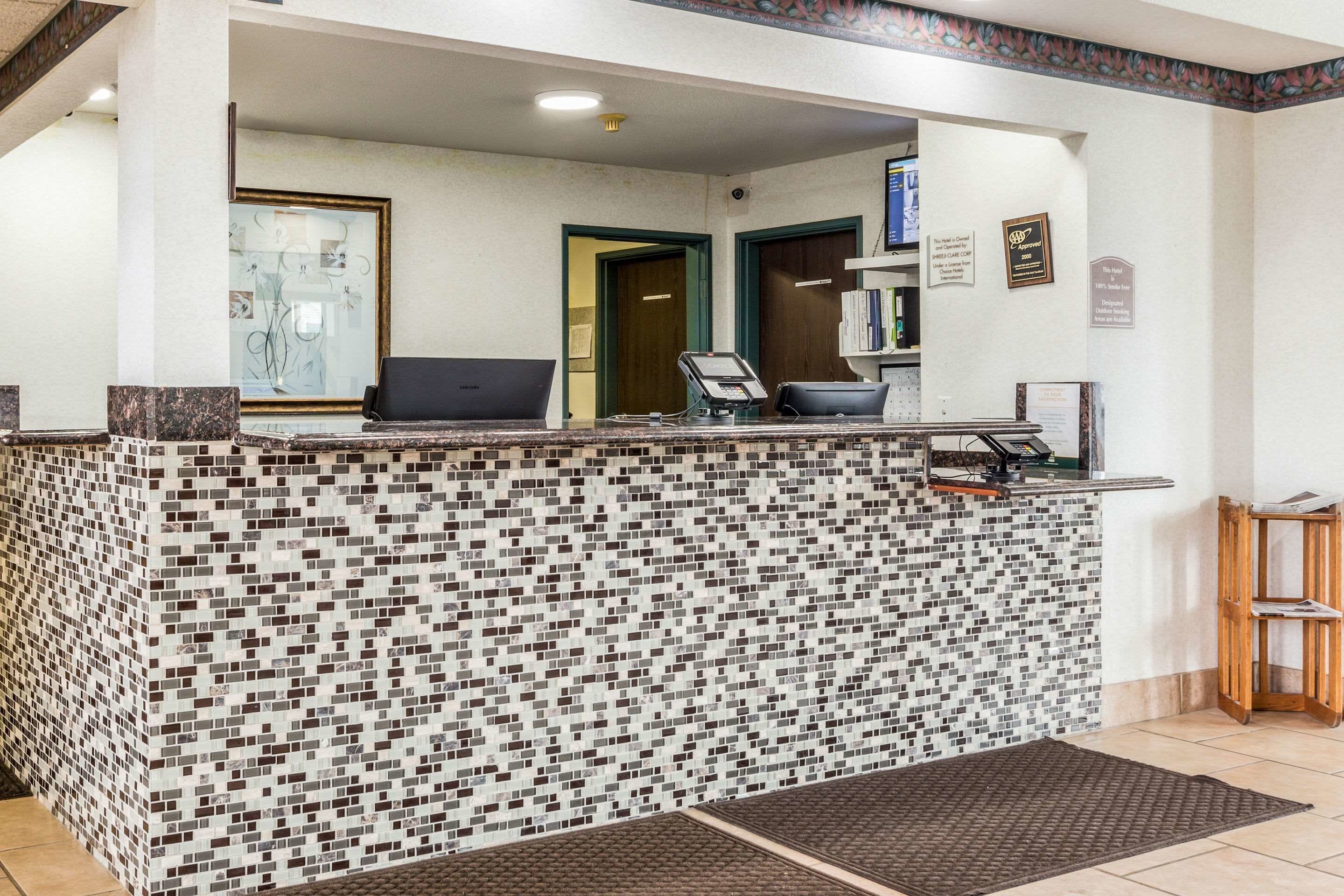 Un área de recepción con pared de mosaicos, un mostrador de recepción y una computadora.
