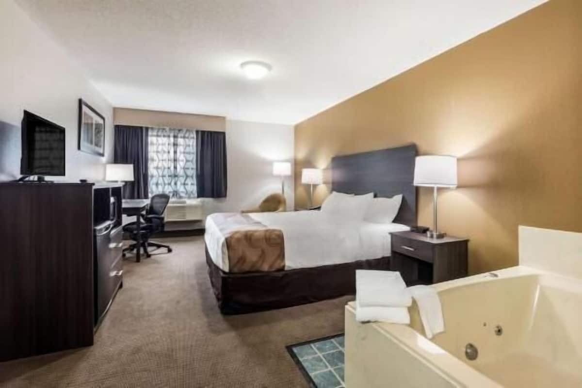 Una habitación de hotel con cama, escritorio, silla, lámparas y una bañera.