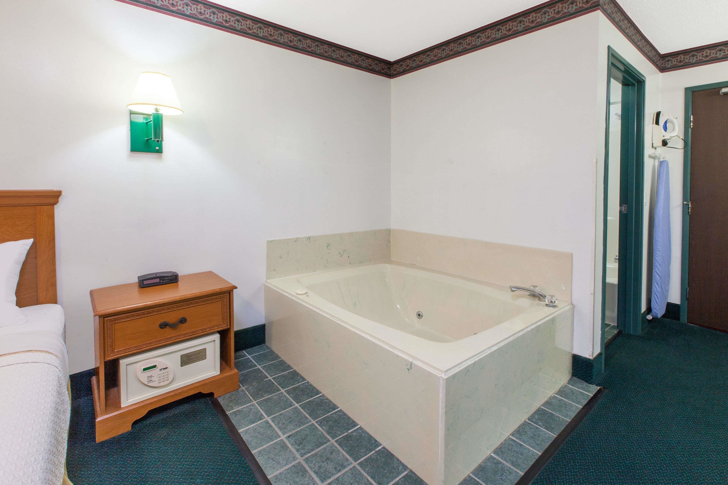 Un baño de hotel con una bañera, una mesita de noche con un control remoto y una lámpara de pared.