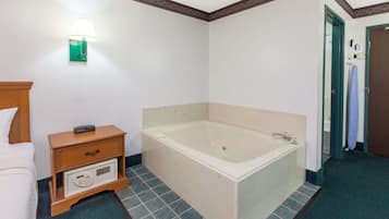 Um banheiro de hotel com banheira, uma mesinha de cabeceira com controle remoto e um luminário fixado na parede.