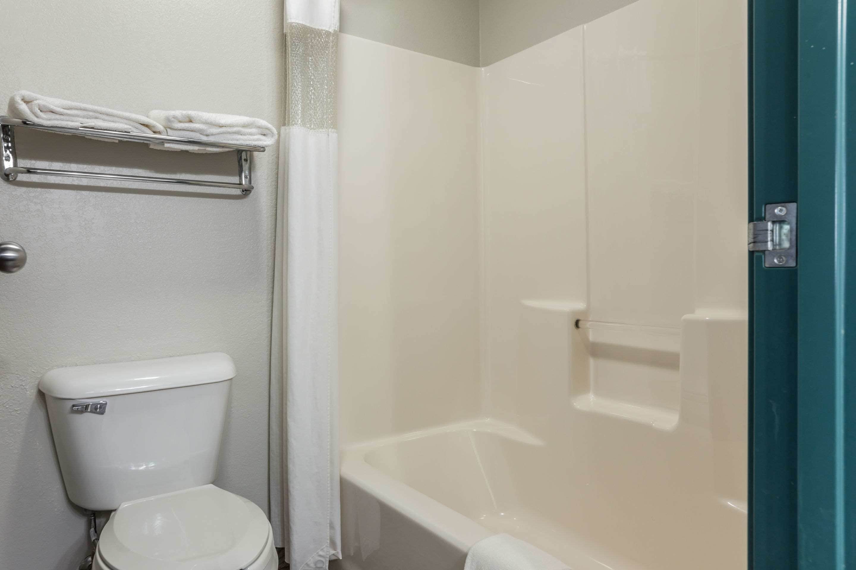 A bathroom with a toilet, a towel rack with folded towels, and a bathtub.