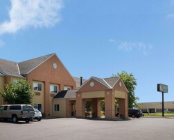 A hotel with a central entrance, multiple windows, and a parking lot with several vehicles.