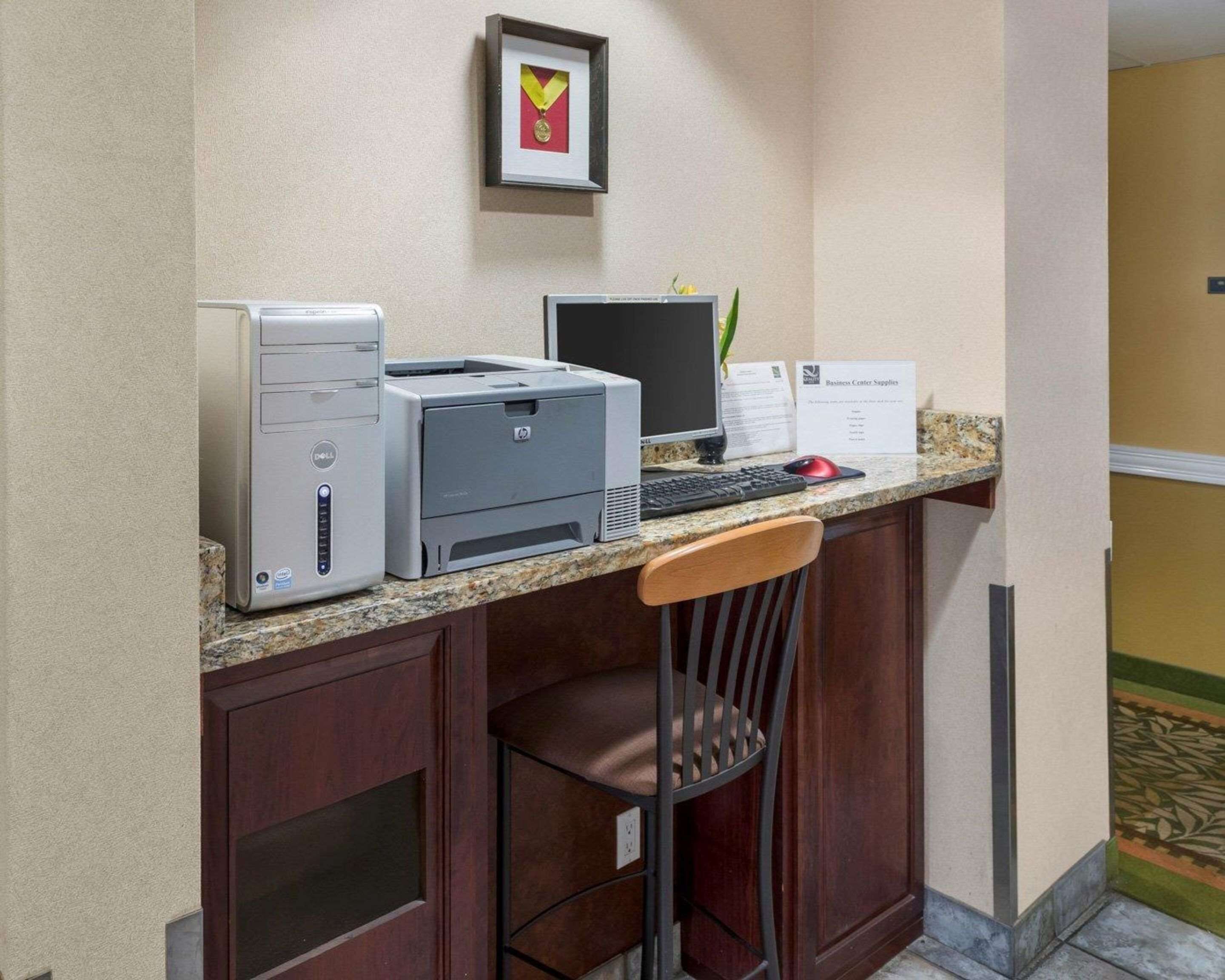 A hotel reception desk with a desktop computer, a printer, and a framed award on the wall.