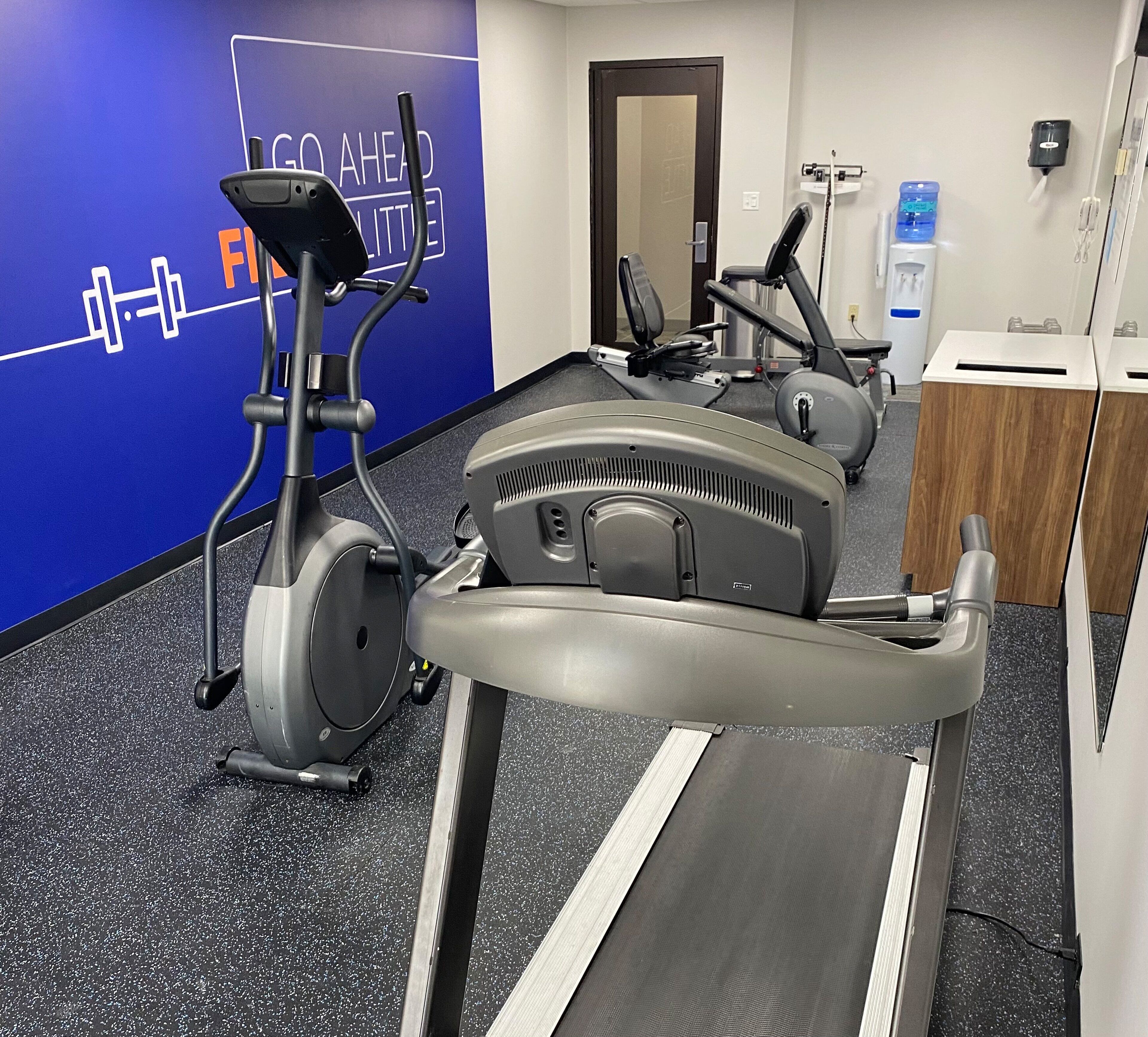 A gym with stationary bikes, a treadmill, and a water dispenser.