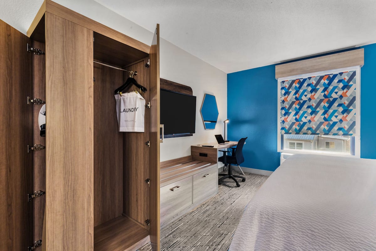 A hotel room with a wooden wardrobe, a desk with a laptop, a chair, and a bed.