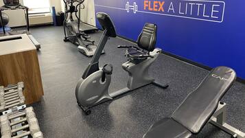 A gym with cardio machines, dumbbells, and a wall with motivational text.